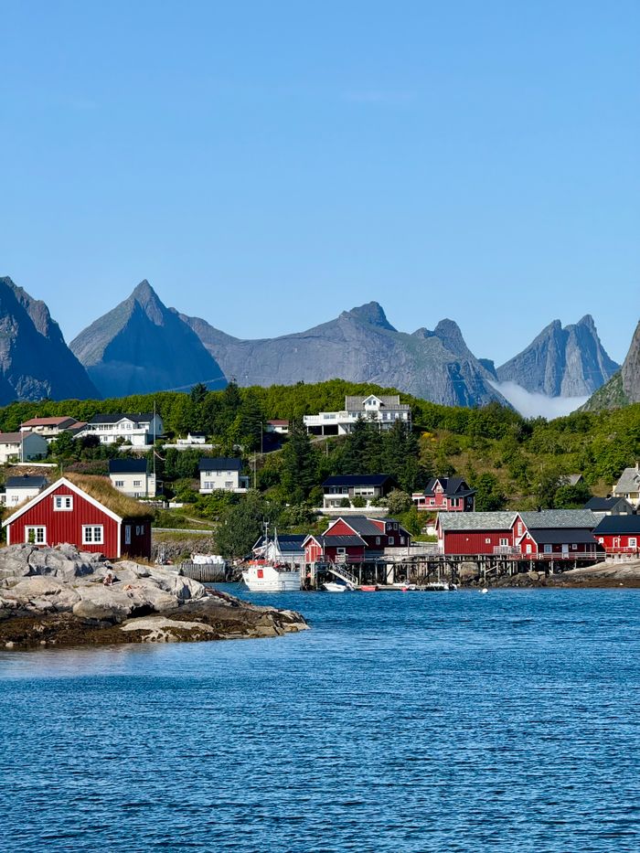 Picturesque view of a fishing village with red cabins in Lofoten, Norway, surrounded by steep mountains.